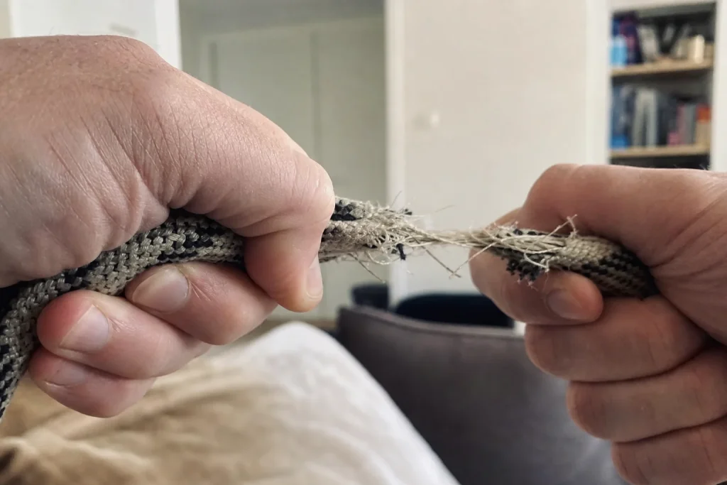 Två händer håller hårt i varsin ände av ett slitet rep i ett vardagsrum, artikel om att barn som slås lättare blir mobbare.