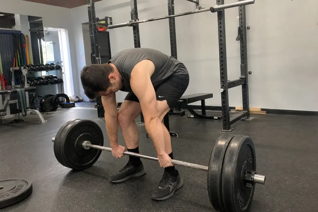 Person som lyfter skivstång med något felaktig teknik i ett gym, ett vanligt träningsögonblick fångat med mobilkamera.