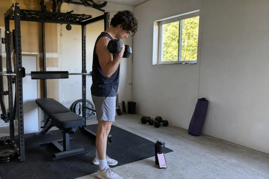 Person tränar med hantel i garagegym och kollar tränings-app, ett exempel på träningstrender Sverige