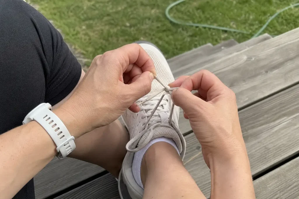 Närbild på händer som knyter upp skosnören på en trätrappa efter soft wellness träning