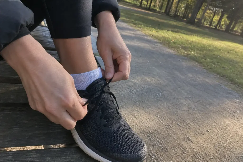 Person snörar en löparsko på böjt knä i morgonljus, kan gälla besvär med ont i knät före joggingpasset.